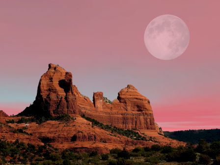 A rocky landscape with red cliffs under a pink sky and a large full moon in the background, creating a serene and majestic scene.