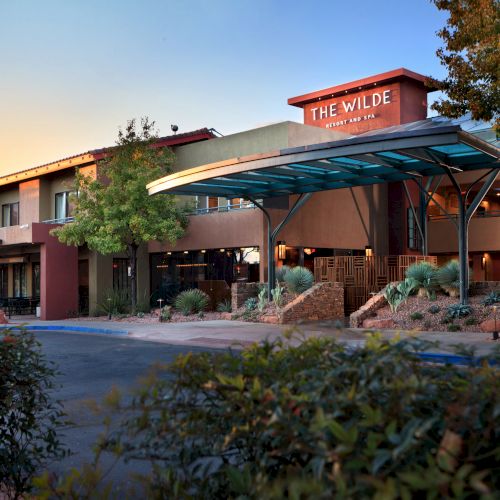 The image shows a modern building with a sign reading "The Wilde Resort and Spa," featuring a distinctive entrance and surrounded by greenery and trees.