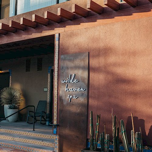 The image shows the entrance to "Willows Spa," featuring a rustic sign, potted plants, and a shaded seating area.