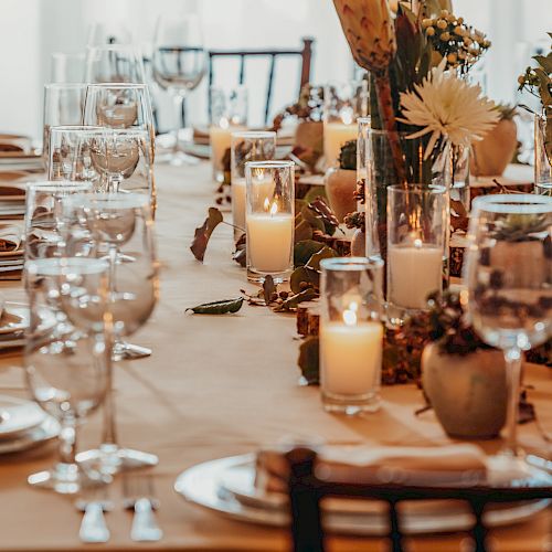 A long table is elegantly set with plates, glasses, napkins, and lit candles, adorned with floral decorations for a formal gathering or dinner.