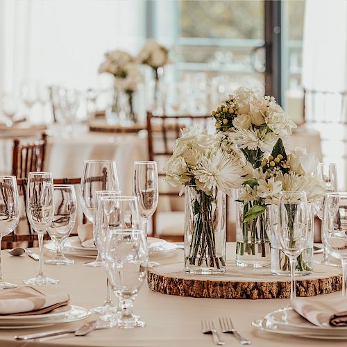 A beautifully set dining table with floral centerpieces, surrounded by elegant tableware and glasses, ready for a formal event or dinner.