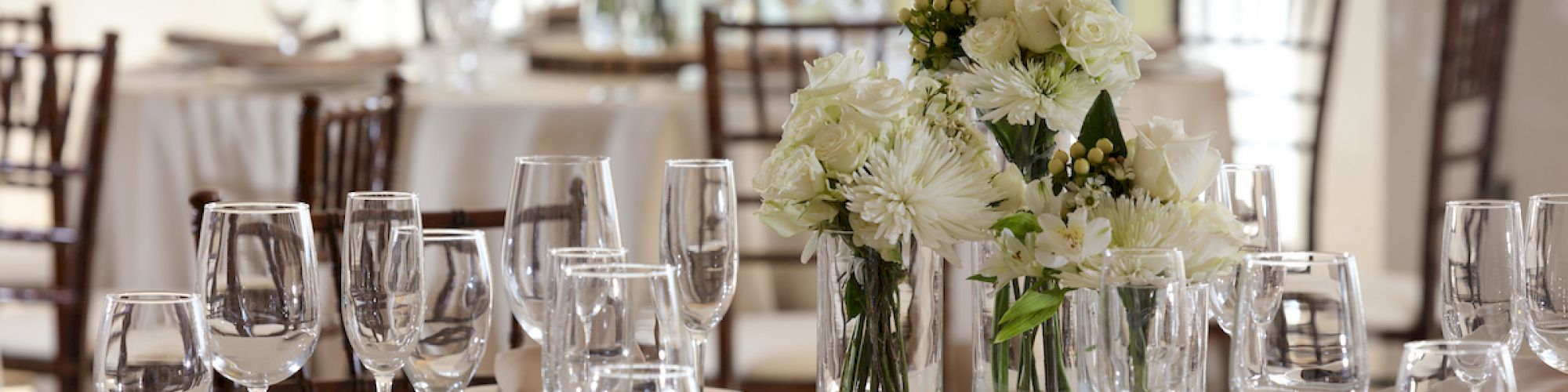 A beautifully set table with white flowers as the centerpiece, accompanied by neatly arranged glasses, plates, and cutlery in an elegant dining setting.