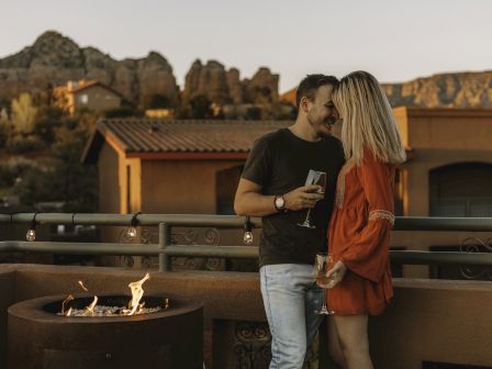A couple enjoying a moment on a terrace with a fire pit, holding wine glasses, surrounded by a scenic mountainous backdrop.