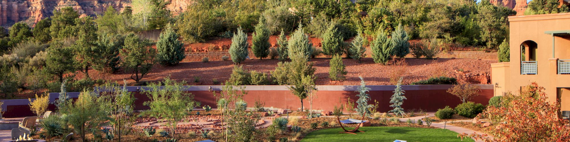 A scenic landscape with pathways, a garden, and trees, set against a backdrop of mountains under a blue sky.
