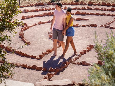 A couple walks through a path bordered by rocks, surrounded by a natural setting with plants.